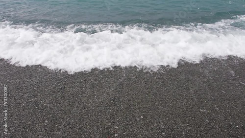 Sea tide on a pebble shore. Waves with white foam on a pebble beach. Nature concept, vacation, background