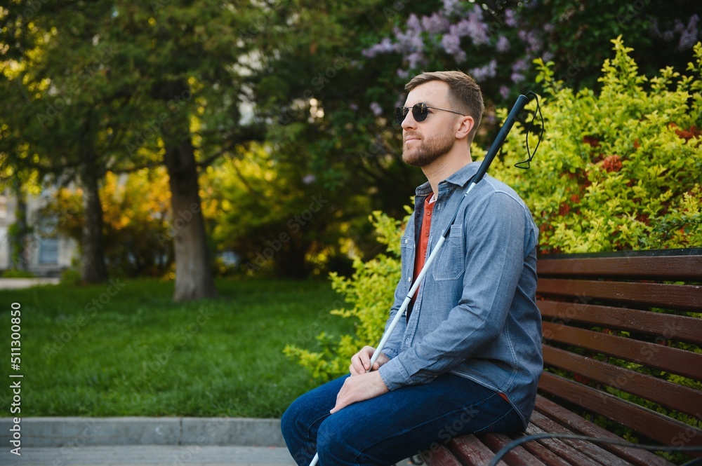Visually impaired man with walking stick, sitting on bench in city park. Copy space Visually impaired man with walking stick, sitting on bench in city park. Copy space