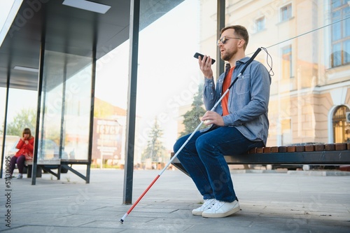Photographie blind man with white cane waiting for public transport in city.