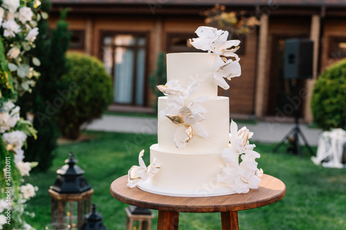 Front close up view of beautiful minimalist wedding cake in white color cream decorated with rose petals decor. Wedding concept. 
