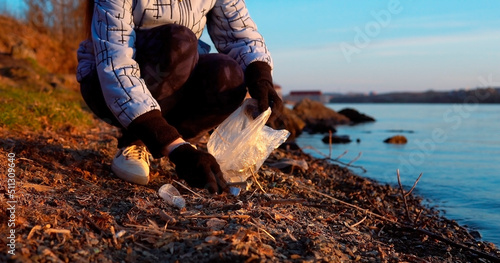 Woman volunteer collects garbage on the see shore in the evening at sunset
