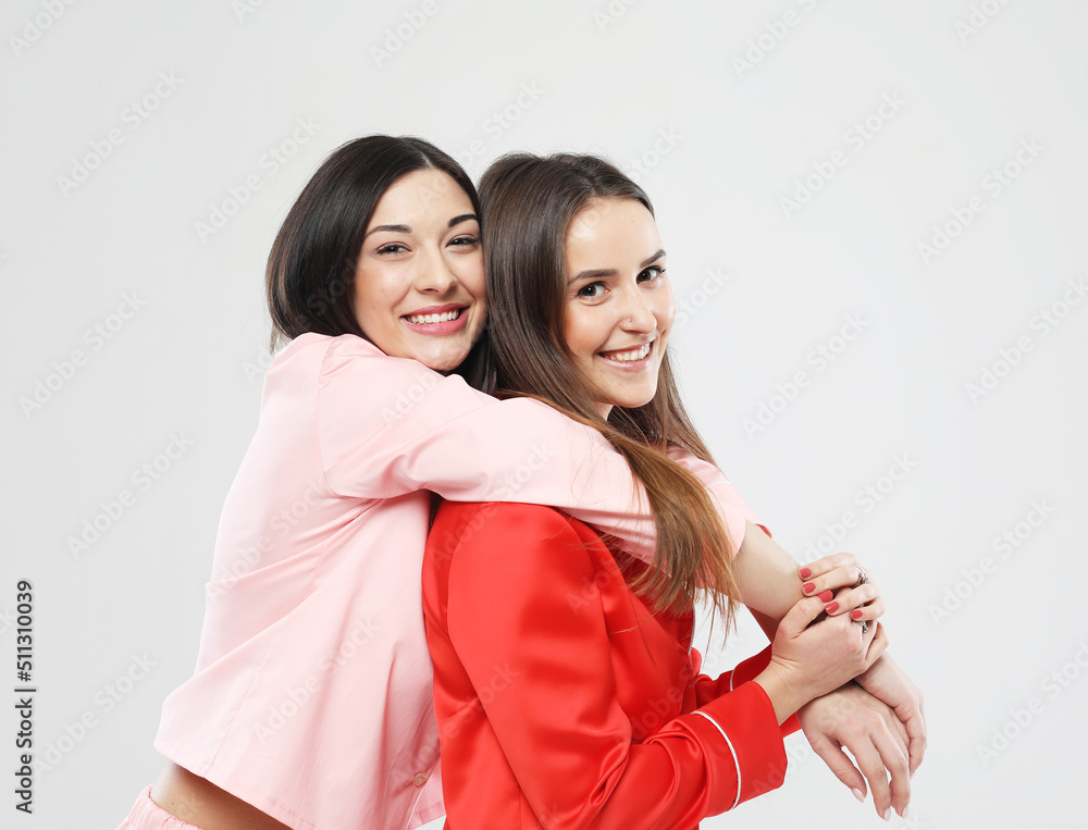 two beautiful females friends dressed in pajamas hugging and smiling over white background two beautiful females friends dressed in pajamas hugging and smiling over white background