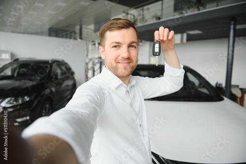 Young man is choosing a new vehicle in car dealership and making photo on a smartphone.
