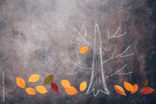 Sketch of an autumn tree with fallen colorful leaves on a dark rustic background. Tree drawn in chalk. Creative layout.