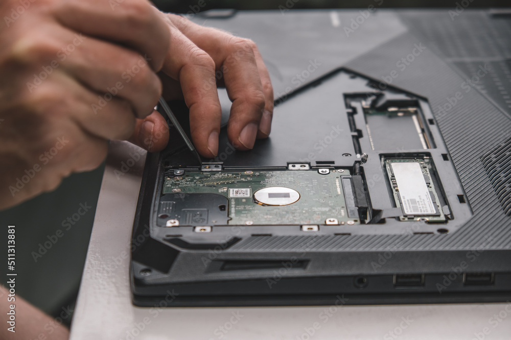 Obraz premium close-up of repairman's hands removing hard drive from laptop case with screwdriver for repair and maintenance. unscrew the screws with a screwdriver. laptop repair and maintenance. selective focus.