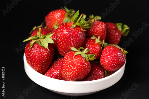 Fototapeta Naklejka Na Ścianę i Meble -  Red fresh strawberries in a white plate on a black background. Summer seasonal berries, close-up