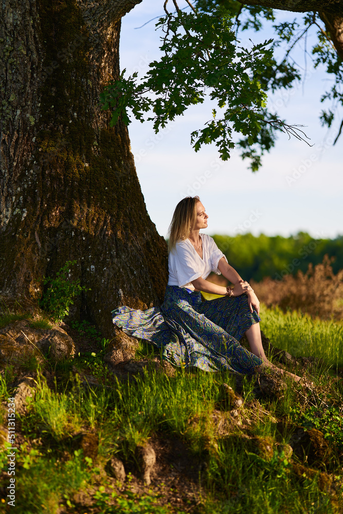Fototapeta premium Young woman posing at sunset by an oak tree