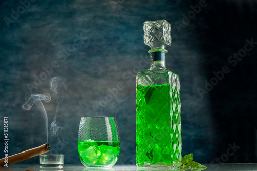 green mint drink in elegant vintage bottle on lighted bar counter with cigar with smoke photo