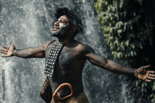 Close-up of Papua man of Dani tribe spread out his hands feel freedom, against waterfall at greenery forest