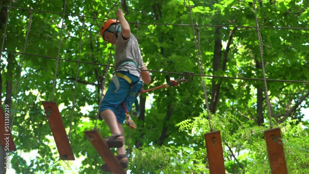 Rope park. A boy teenager in a helmet walks on suspended rope ladders ...