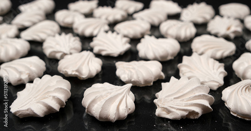 White meringues on a black background, sweet pastries, a dessert of sugar and egg white.