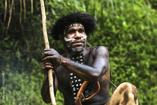 Portrait of Dani Tribe man wearing koteka, traditional clothes of Papua. Dani tribe men looking around and ready to hunt animal prey in the jungle.  photo