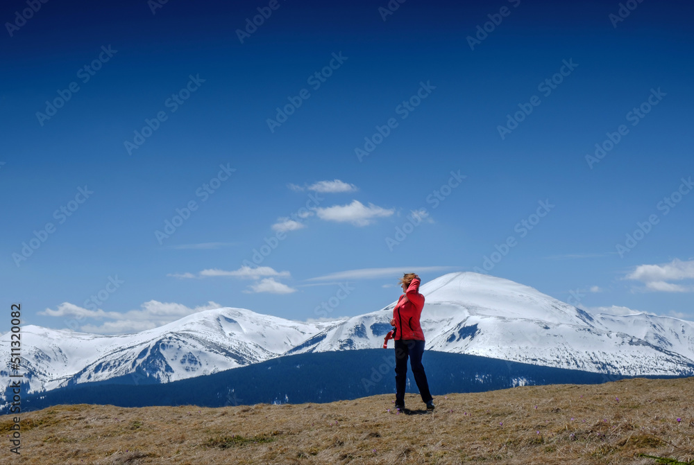 Obraz premium A young girl at the top of the mountain looks at the snowy mountains in the background