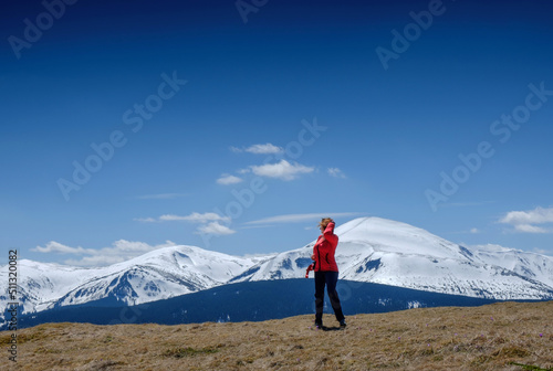 A young girl at the top of the mountain looks at the snowy mountains in the background