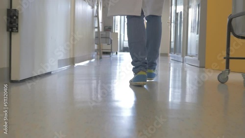 Legs of lab worker in jeans and sneakers walking in lab corridor. Tracking shot.