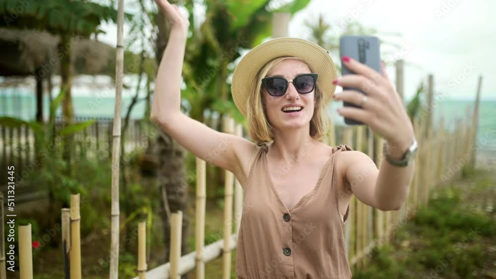 Cheerful beautiful girl in a summer hat and glasses calls for a video call on the background of the sea. Video call from vacation. Cheerful beautiful girl in a summer hat and glasses calls for a video call on the background of the sea. Video call from vacation.