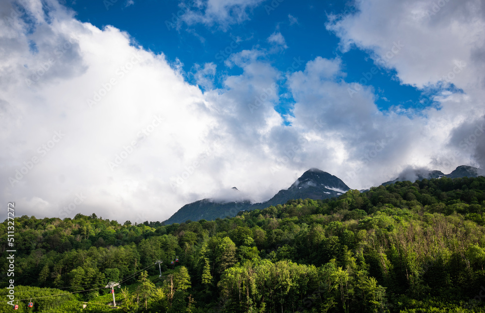 Great view of the mountains. Leisure and outdoor recreation. Summer view of the Caucasus mountains, green mountains and white clouds in the blue sky. Cable car in the mountains.