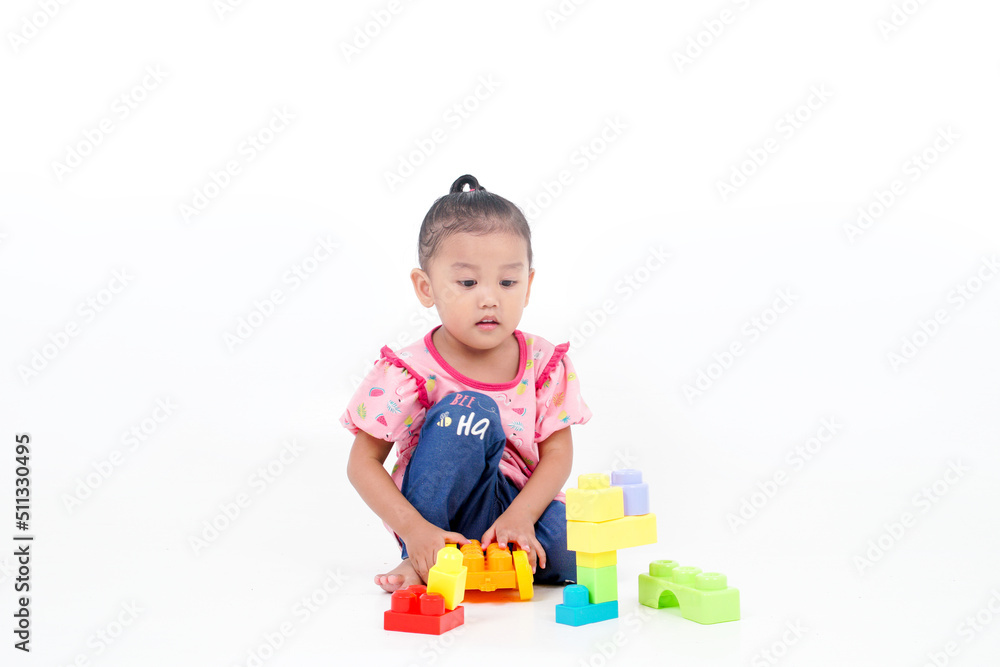 Lovely little cute asian girl playing on the floor with lots of colorful plastic blocks in studio, isolated on white background Lovely little cute asian girl playing on the floor with lots of colorful plastic blocks in studio, isolated on white background