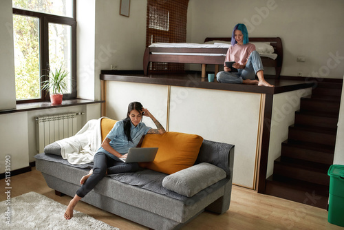 Girl using tablet while girlfriend watching laptop