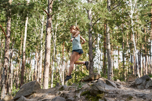 Side view of sportswoman running on hill in forest