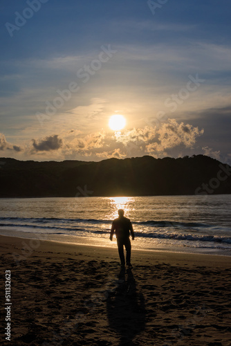春の伊豆の弓ヶ浜で朝日にきらめく海に向かって歩く男性