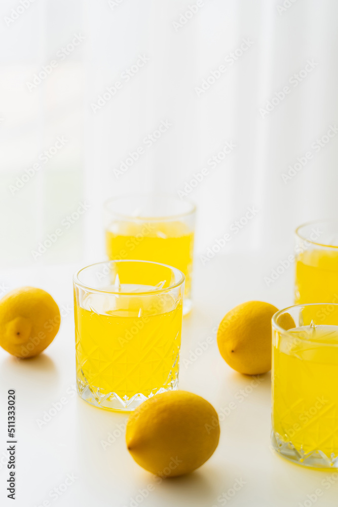glasses with natural lemonade near whole lemons on white and blurred background. glasses with natural lemonade near whole lemons on white and blurred background.