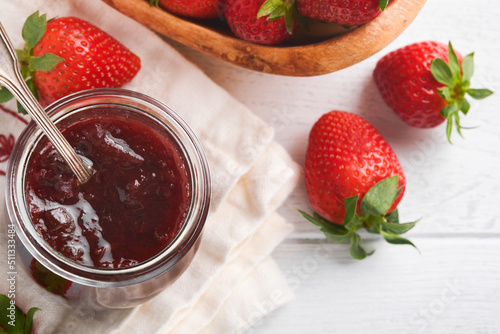 Strawberry jam. Strawberry jam in glass jar with fresh berries plate on white wooden table background, closeup. Homemade strawberry fruity jam. Top view with copy space.