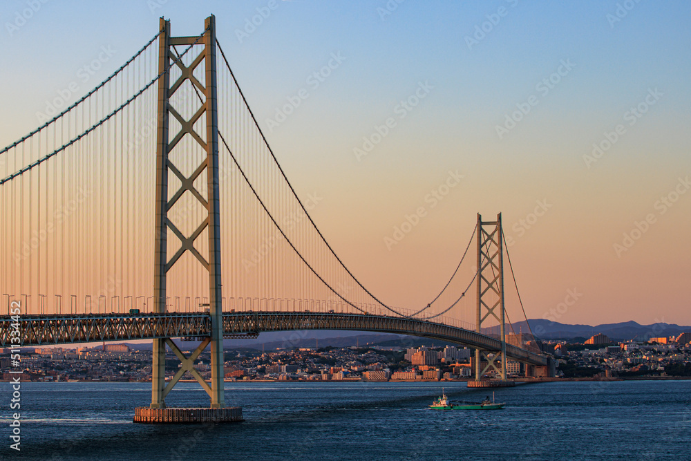 Fototapeta premium Small cargo ship passes under suspension bridge at sunset