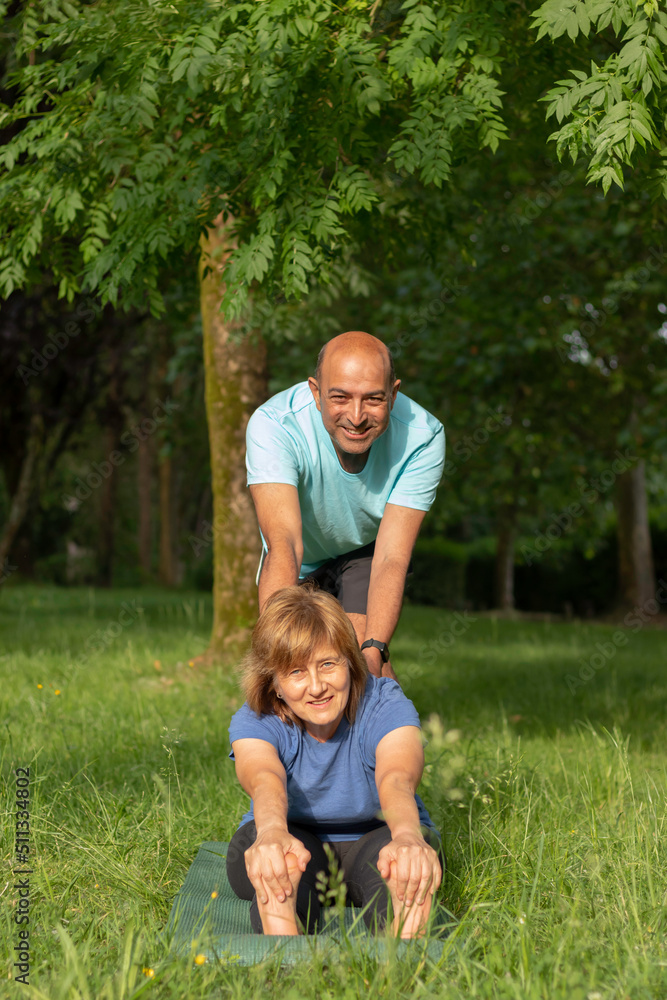 Front vertical view of old couple practising yoga in the park while looking to the camera smiling and happy Front vertical view of old couple practising yoga in the park while looking to the camera smiling and happy