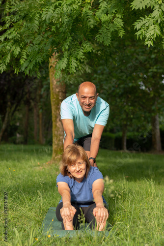Front vertical view of old couple practising yoga in the park while looking to the camera smiling and happy