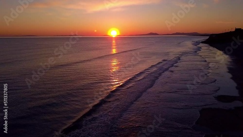 Slow Motion reverse drone shot of a Welsh beach at sunset with the sun lighting up the breaking waves. photo