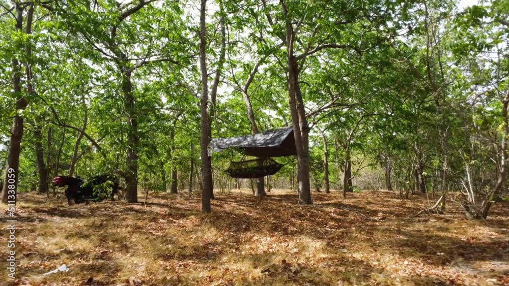 Army Hammock Under The Roof Hanging From The Tree In The Forest. - aerial forward Army Hammock Under The Roof Hanging From The Tree In The Forest. - aerial forward