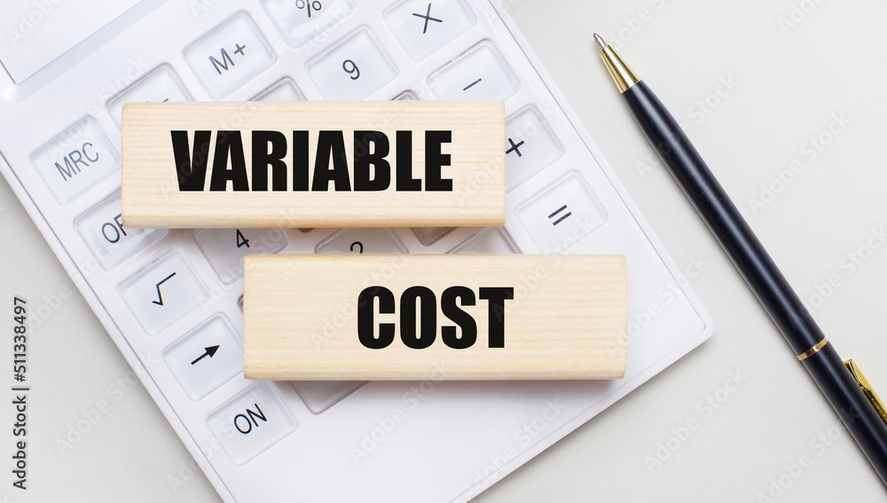 Wooden blocks with the VARIABLE COST Iie on a light background on a white calculator. Nearby is a black handle. Business concept Wooden blocks with the VARIABLE COST Iie on a light background on a white calculator. Nearby is a black handle. Business concept