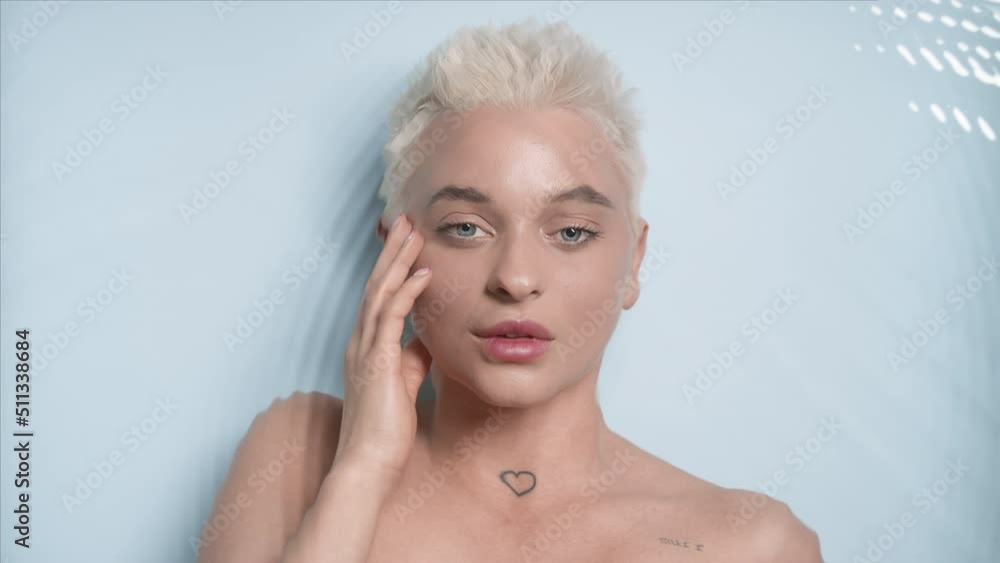 Gorgeous young slim light-haired Caucasian woman strokes her face looking at the camera through rippling water on pale blue background | Acne prevention concept Gorgeous young slim light-haired Caucasian woman strokes her face looking at the camera through rippling water on pale blue background | Acne prevention concept