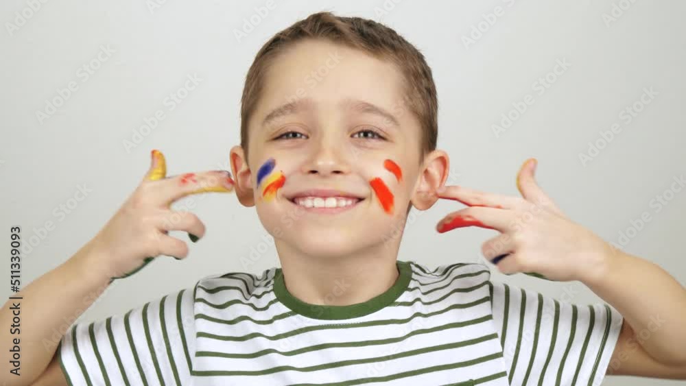 Portrait of a child. The boy shows his hands in watercolors and paints lines on his face. Colors of life Portrait of a child. The boy shows his hands in watercolors and paints lines on his face. Colors of life