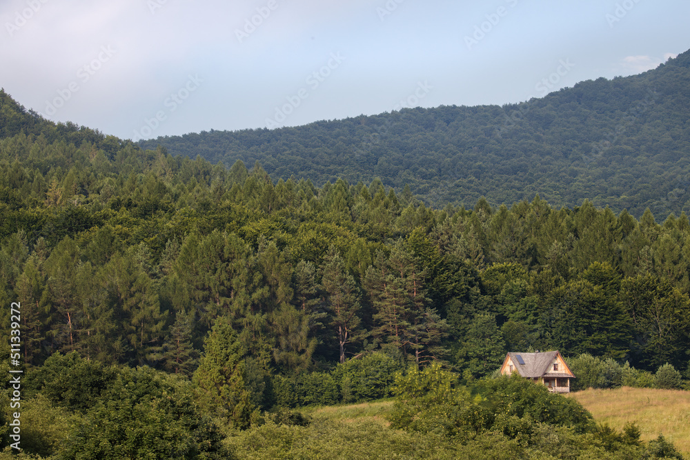 A mountain landscape with a clearing on which stands a wooden house. Beautiful view of nature and a house in a clearing at the foot of the mountains. A romantic sight