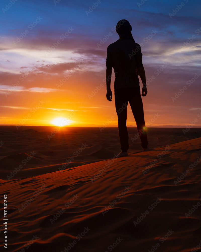 silhouette of person walking in the desert at sunset - Merzouga, Morocco