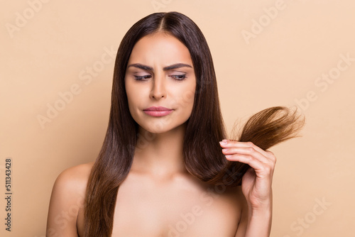 Portrait of attractive suspicious long-haired girl holding dry ends balm mask solution trouble isolated over beige pastel color background