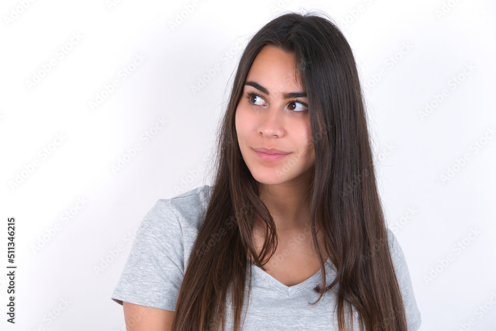 Young beautiful brunette woman wearing grey T-shirt over white wall looking aside into empty space thoughtful Young beautiful brunette woman wearing grey T-shirt over white wall looking aside into empty space thoughtful