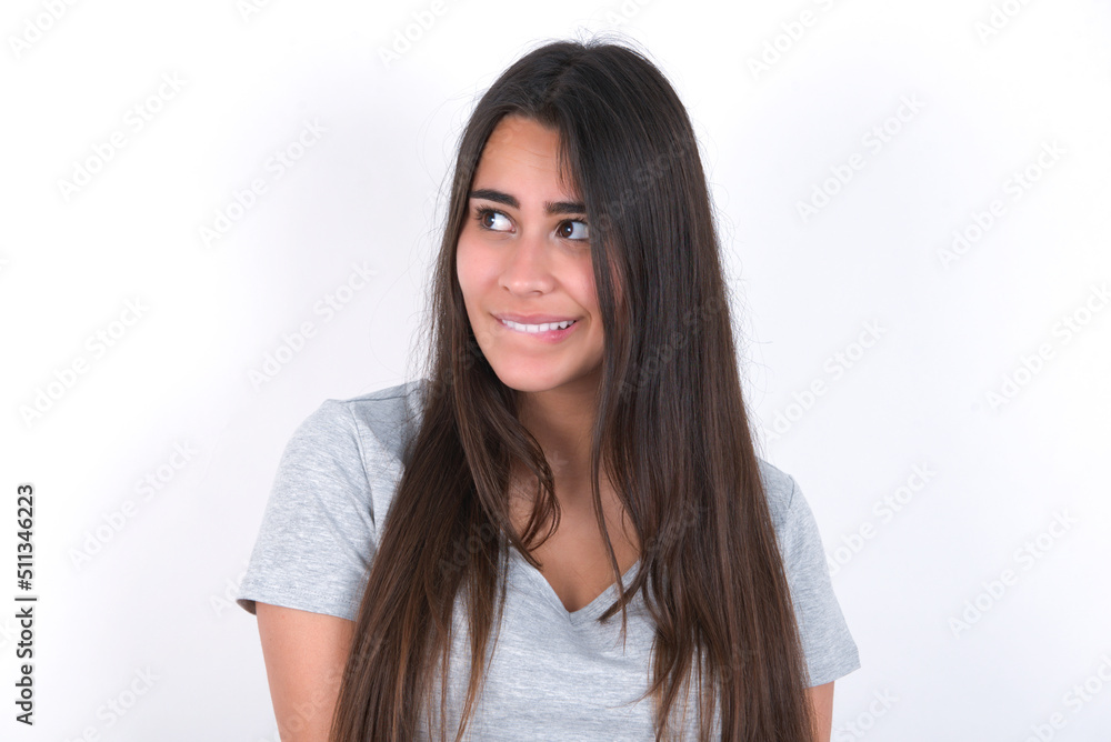 Amazed Young beautiful brunette woman wearing grey T-shirt over white wall bitting lip and looking tricky to empty space. Amazed Young beautiful brunette woman wearing grey T-shirt over white wall bitting lip and looking tricky to empty space.