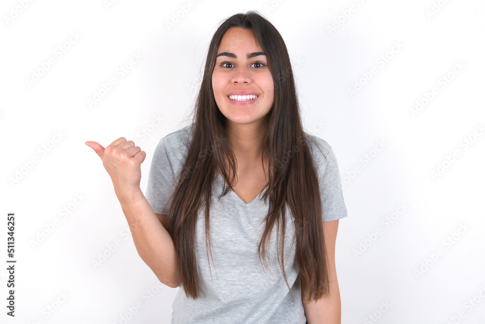 Lovely Young beautiful brunette woman wearing grey T-shirt over white wall pointing aside with forefinger, showing at copy space having news about bargains Lovely Young beautiful brunette woman wearing grey T-shirt over white wall pointing aside with forefinger, showing at copy space having news about bargains