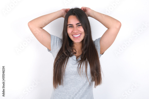 Young beautiful brunette woman wearing grey T-shirt over white wall stretching arms, relaxed position.