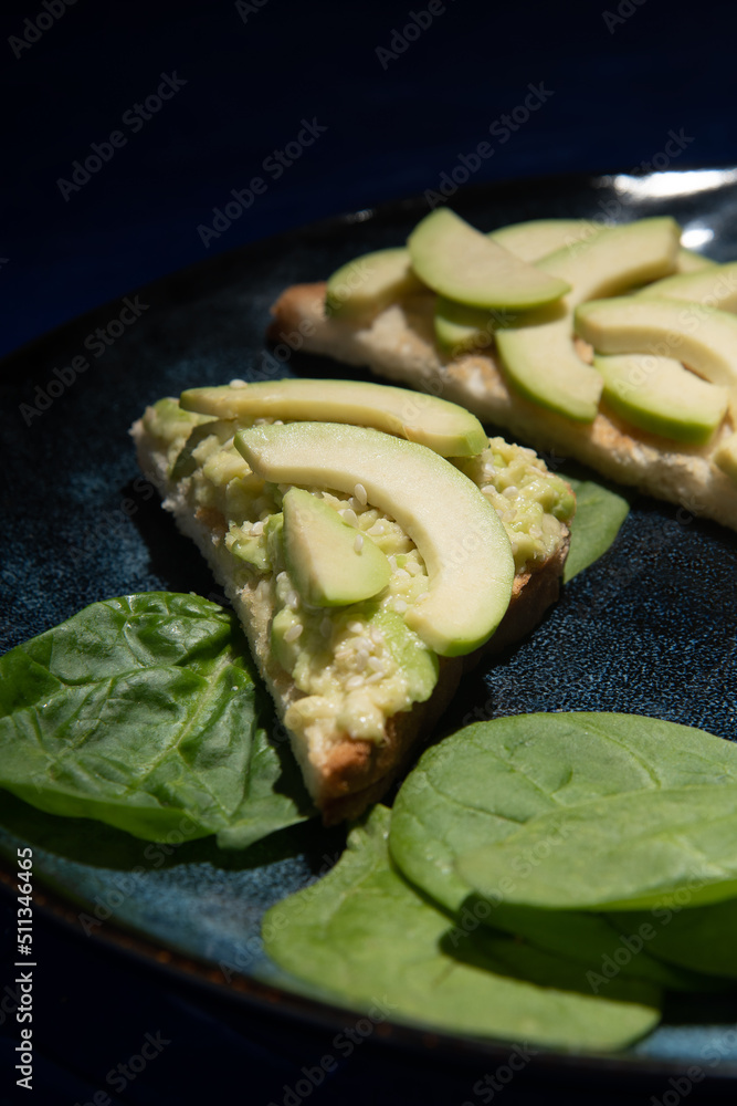 Sandwiches on a plate with avocado and spinach on a dark background. Sandwiches on a plate with avocado and spinach on a dark background.