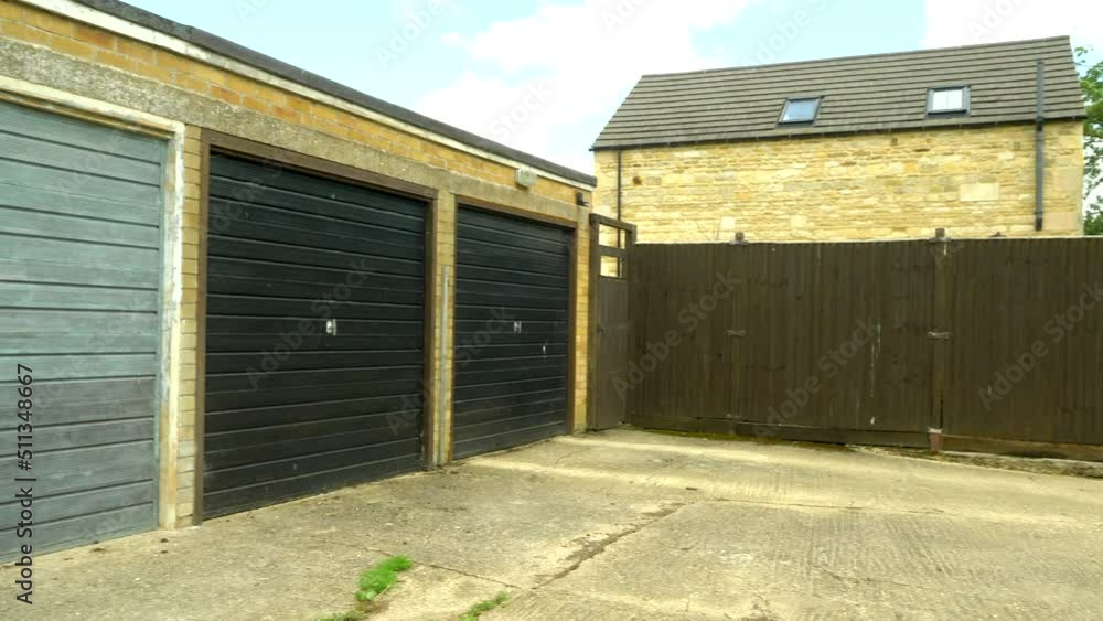 Establishing pan shot of three old lock-up garages, with metal doors, next to a village country lane, in rural England. Establishing pan shot of three old lock-up garages, with metal doors, next to a village country lane, in rural England.