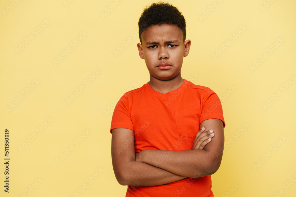 Disappointed young african boy frowning and standing with arms folded Disappointed young african boy frowning and standing with arms folded