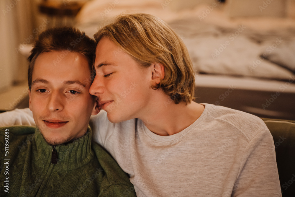Young gay couple hugging and resting on couch while watching tv Young gay couple hugging and resting on couch while watching tv