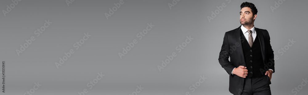 stylish muslim groom in suit posing with hand in pocket while standing isolated on grey, banner. stylish muslim groom in suit posing with hand in pocket while standing isolated on grey, banner.