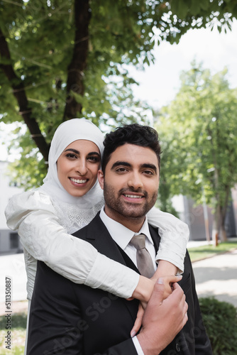 pleased bride in hijab hugging cheerful muslim groom in suit.