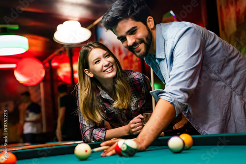 Happy young couple enjoying while playing billiard in bar. People entertainment fun concept photo