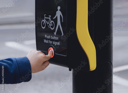 School kid finger pressing  button at traffic lights on pedestrian crossing on way to school. People using traffic signal controlled pedestrian facilities for crossing road